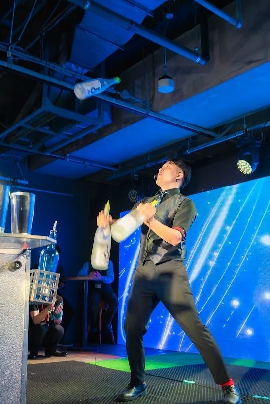 青い照明のステージでボトルをジャグリングするバーテンダー