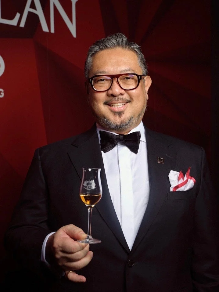 タキシードを着た男性が、ウィスキーグラスを手に笑顔で立っているポートレート