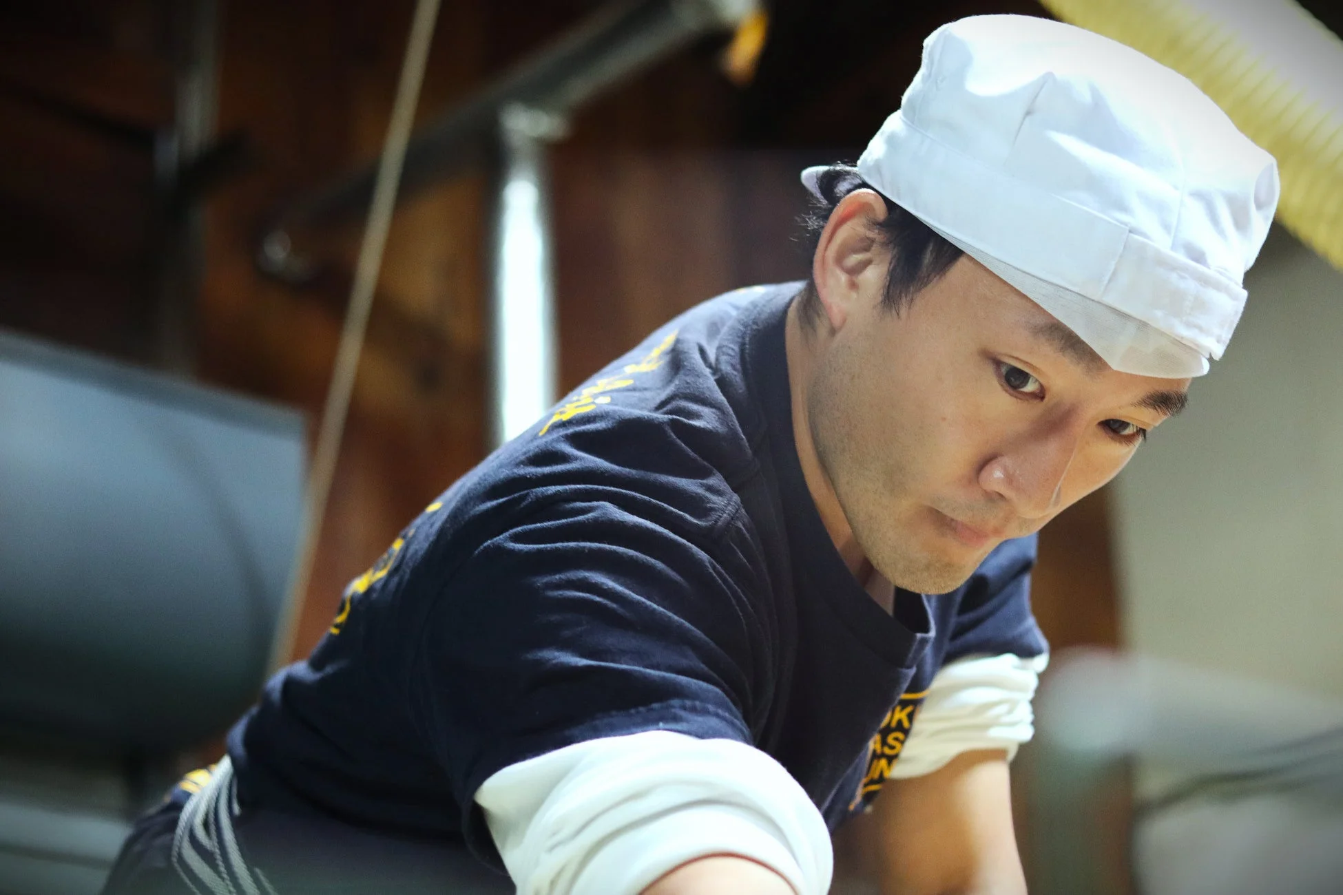 白い帽子をかぶり、紺色の作業着を着た杜氏が真剣な表情で作業に集中しています。