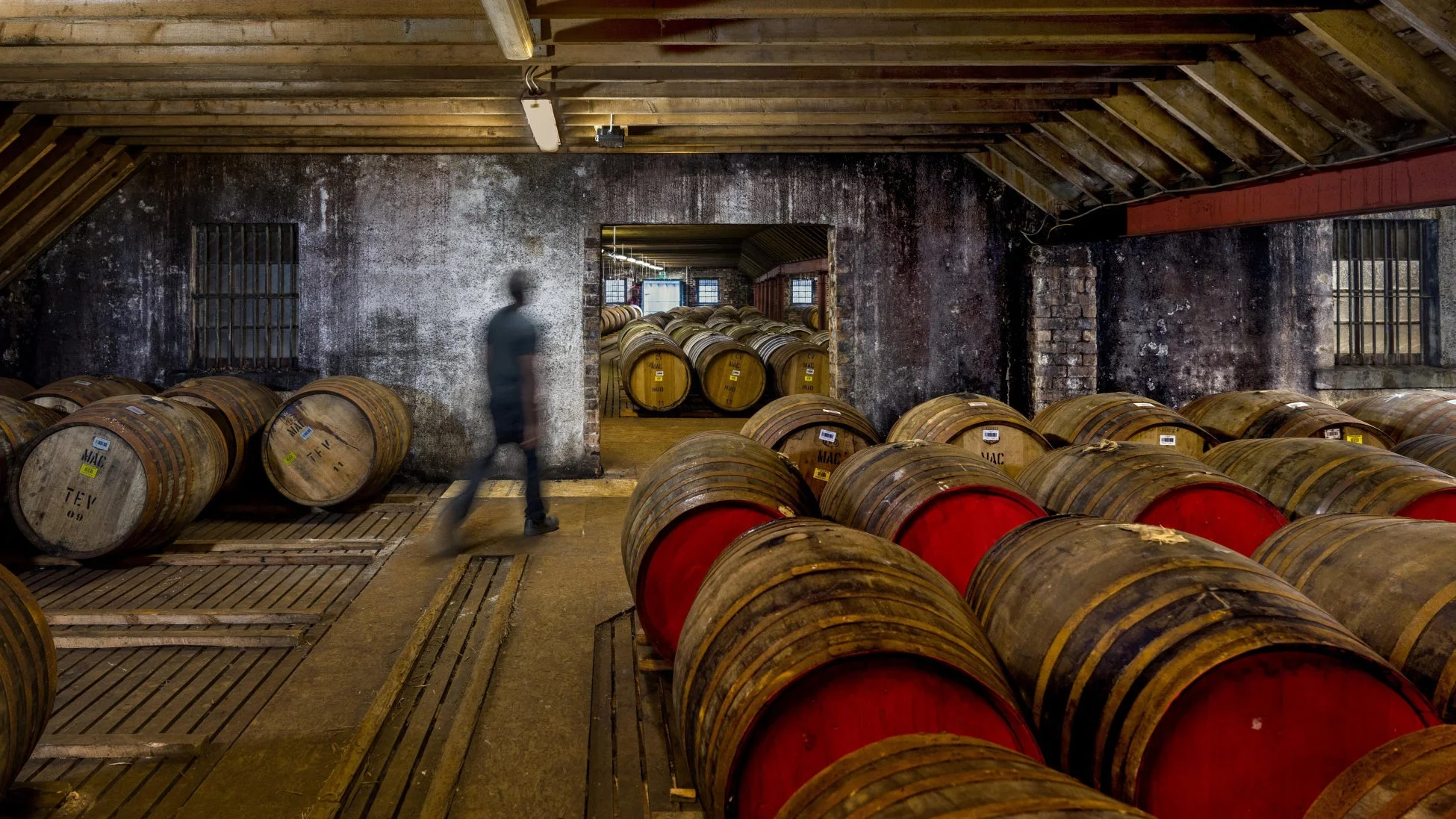 薄暗い熟成庫で、赤く塗られた蓋の木樽が多数並べられています