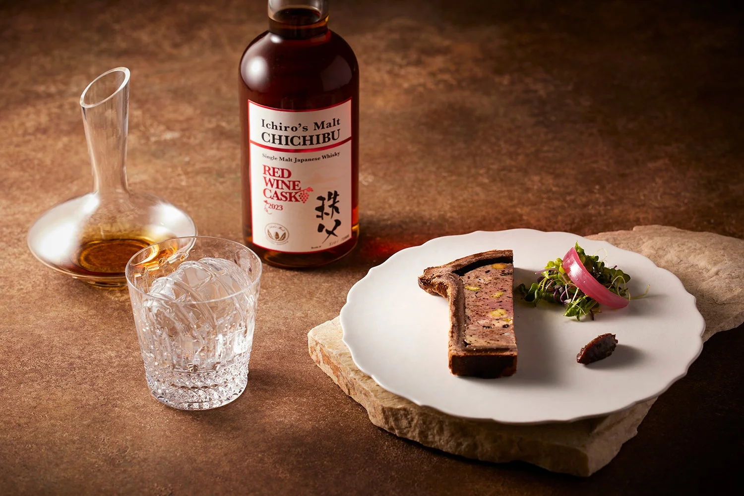 イチローズモルト秩父レッドワインカスクのボトル、グラス、デカンタが写っています。隣にはパテアンクルートとサラダが盛り付けられた料理があり、ウイスキーと料理のペアリングを表現した高級感のある一枚です。
