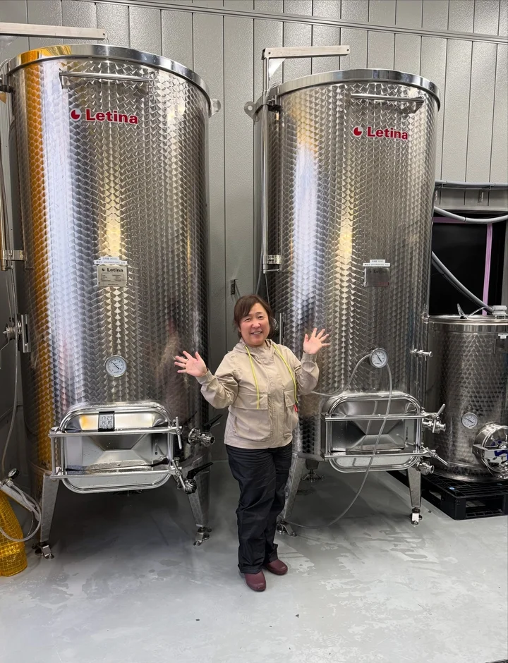 ステンレス製の大型醸造タンクが並ぶ施設で笑顔の女性