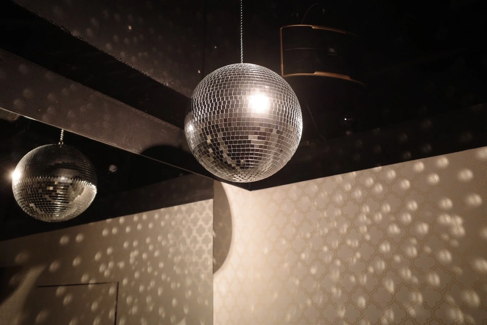 薄暗い空間に大小2つのミラーボールが吊るされており、壁には光の反射による模様が映し出されています。天井にはスピーカーも見えます。