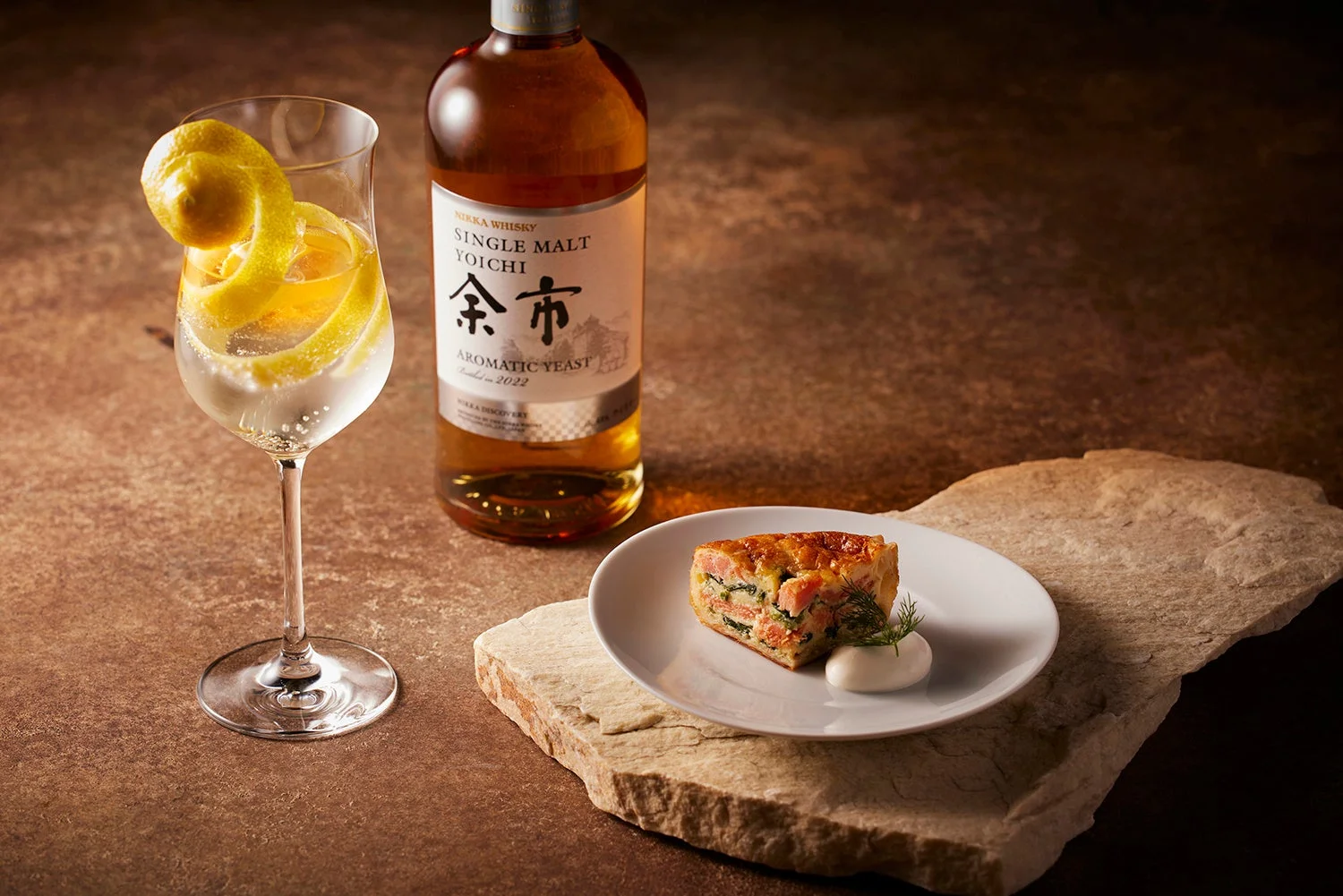 ニッカウヰスキーのシングルモルト余市と、レモンピールが飾られたハイボール、そしてサーモンとほうれん草のキッシュが並べられた、食欲をそそるテーブルフォトです。