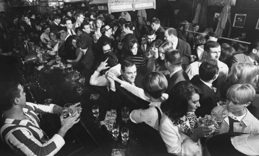 大勢の客で賑わうバーカウンターの様子を捉えたモノクロ写真。