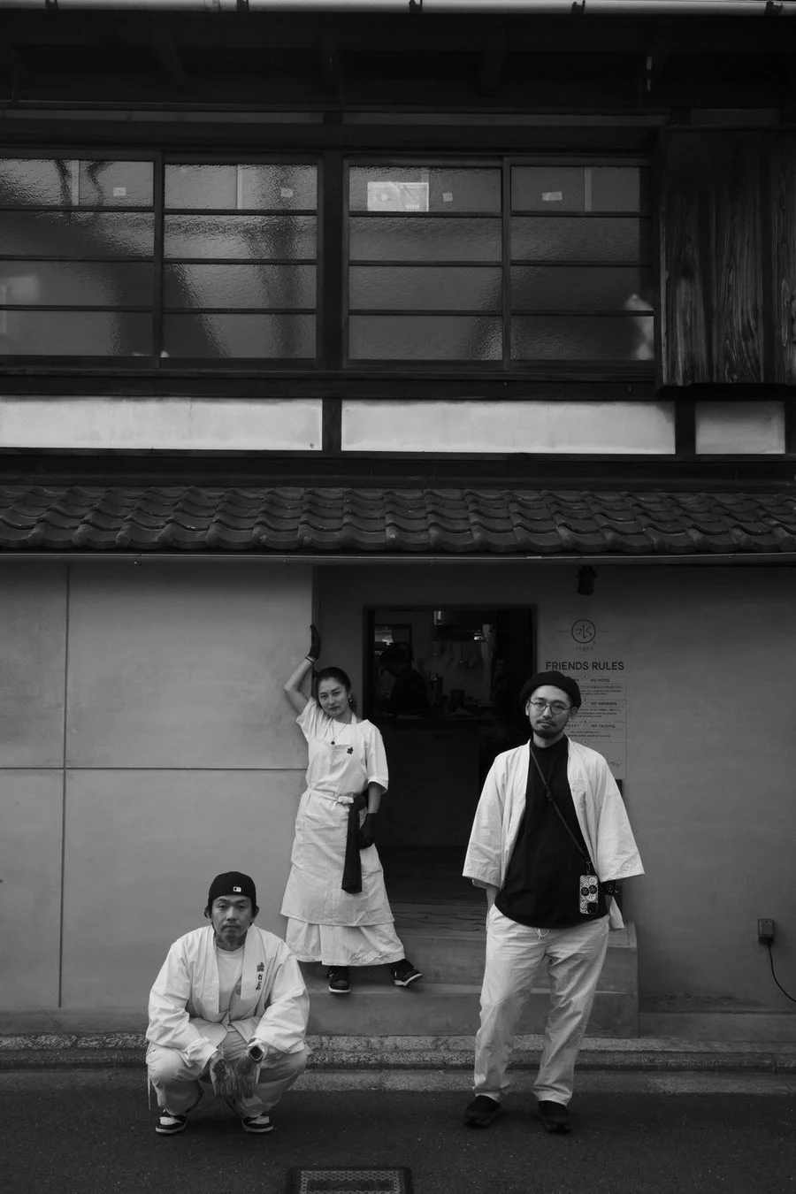 伝統的な日本家屋のような建物の前に立つ3人の人物