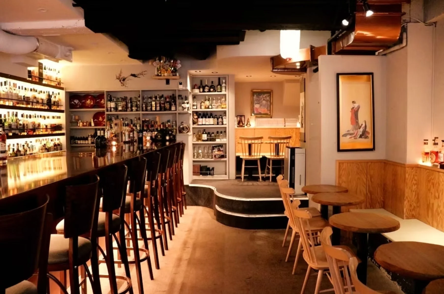 落ち着いた照明のおしゃれなバーの店内。長いカウンター席には多数の酒瓶が並び、奥にはテーブル席も配置されています。洗練された雰囲気で、ゆったりと過ごせる空間が広がっています。