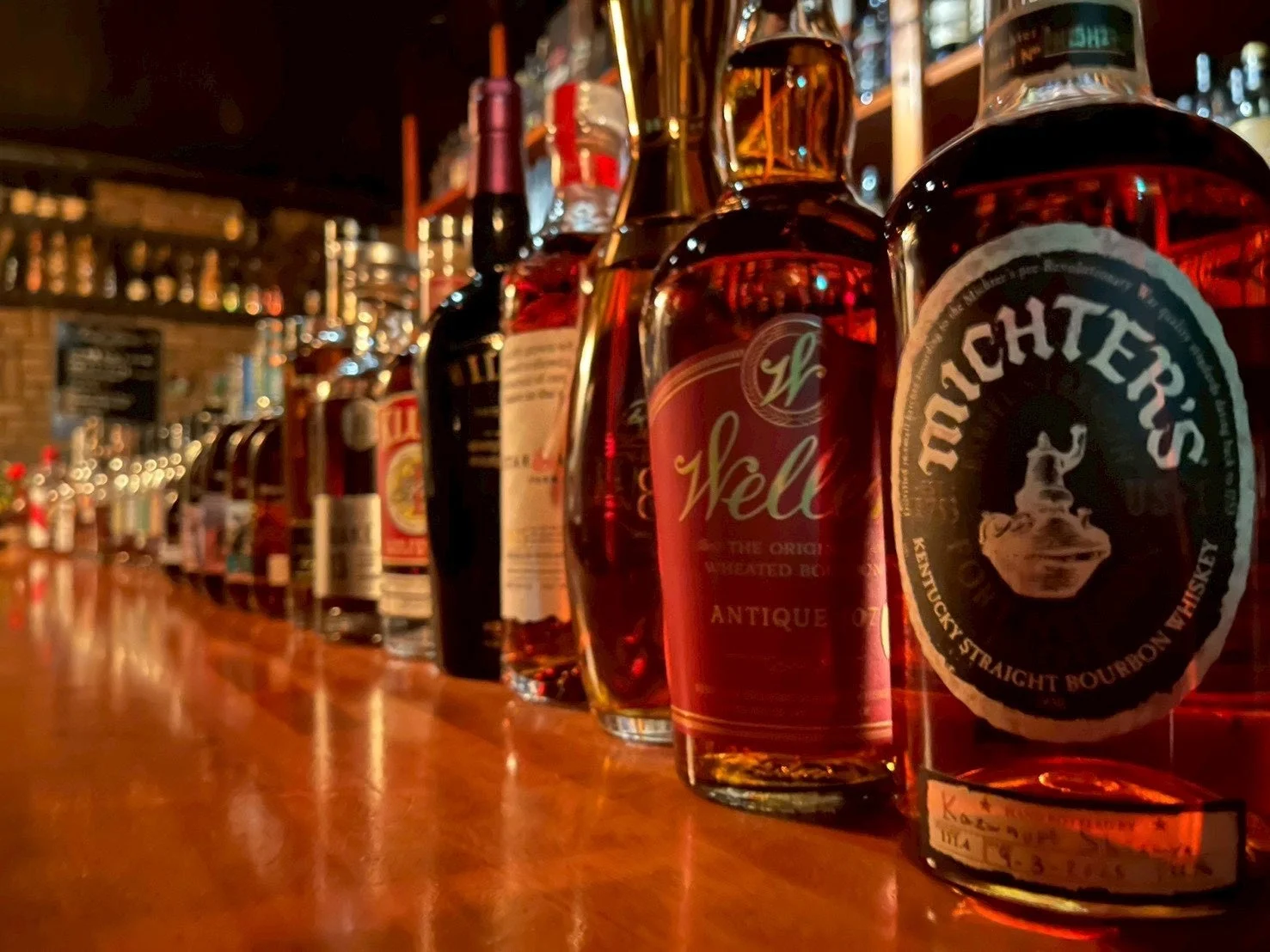 薄暗いバーの木製カウンターに、ミクターズなどのウイスキーボトル