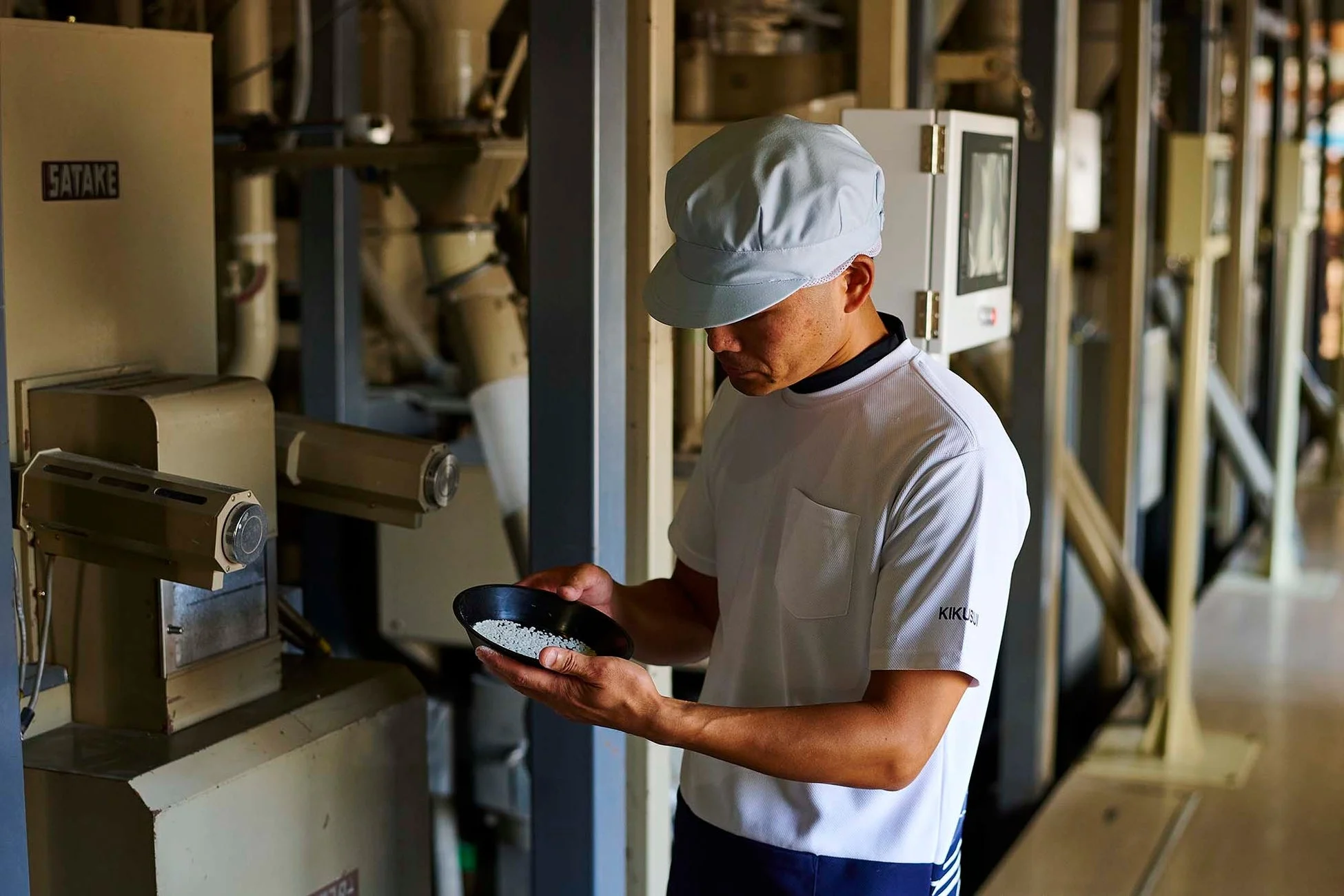精米機が並ぶ工場で米粒を検査する作業員