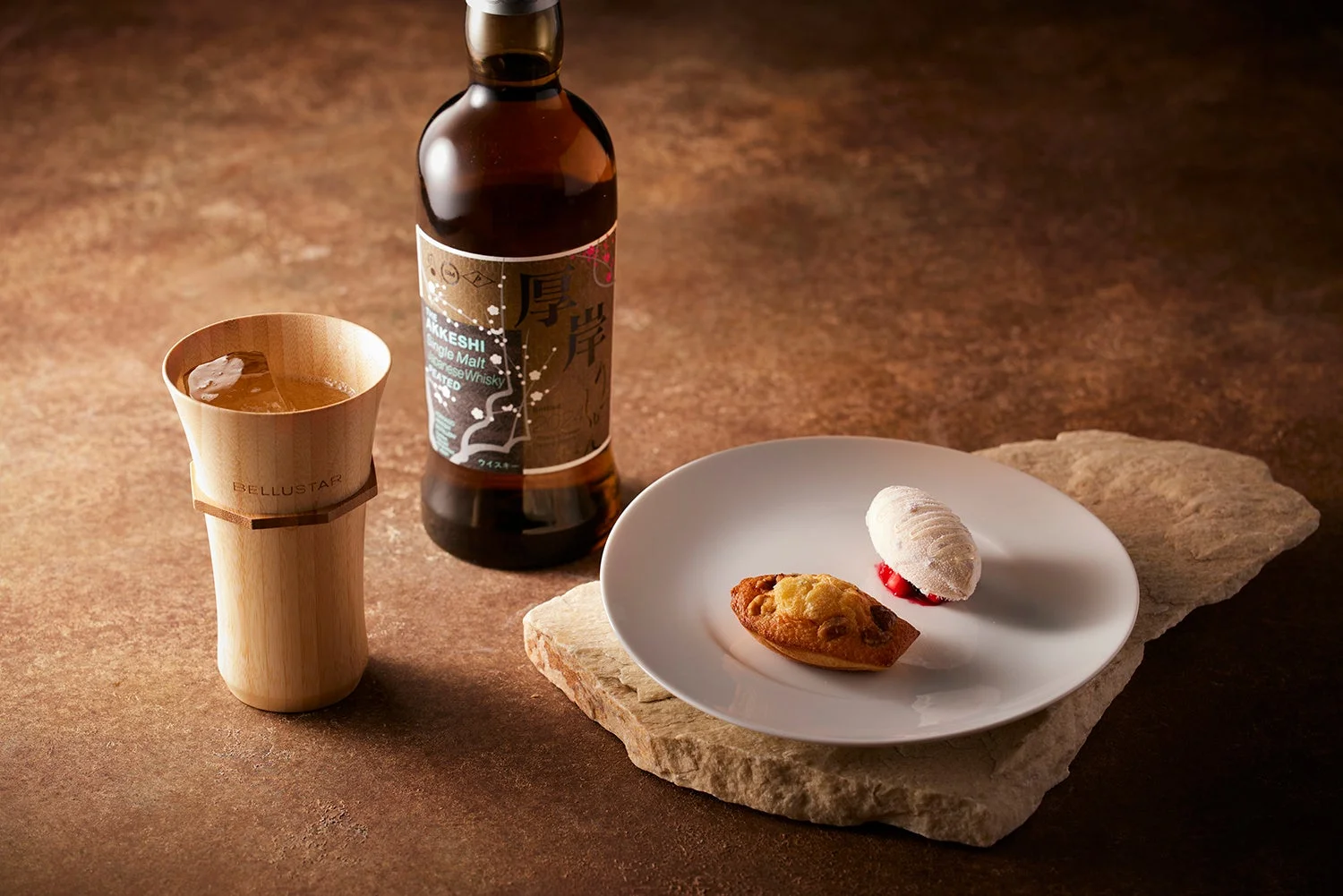 厚岸シングルモルトウイスキーのボトルと木製カップのドリンク、そしてマドレーヌと白いデザートが皿に盛られています。ウイスキーとスイーツの高級感あるペアリングの様子です。