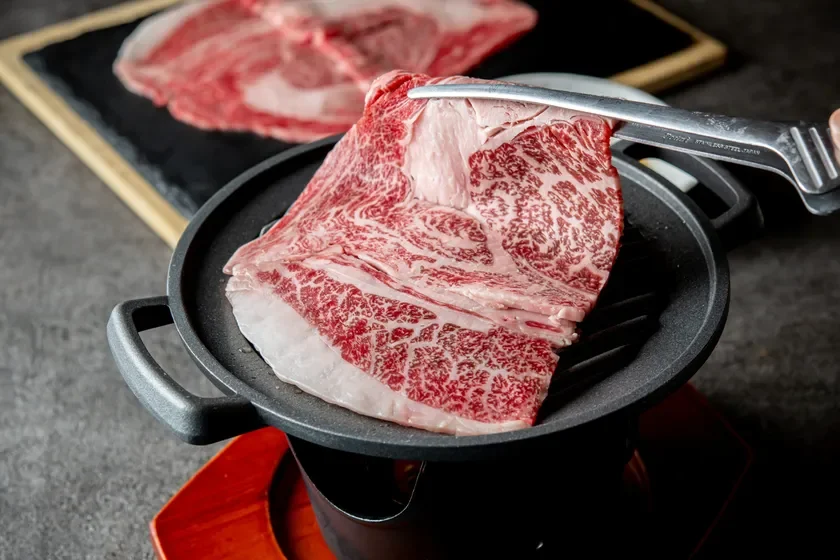美しく霜降りの入った生肉がトングで熱いグリルパンに置かれようとしている