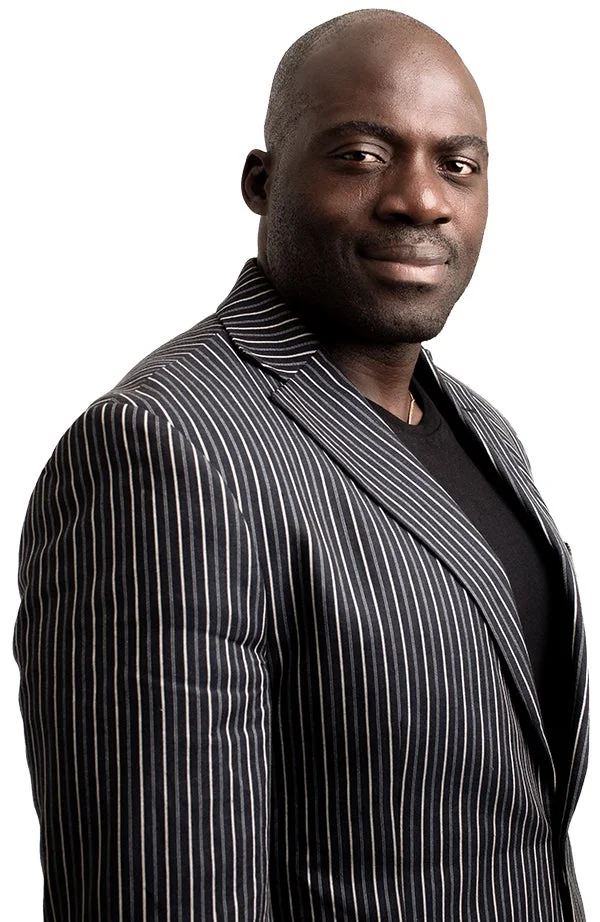 黒いピンストライプのブレザーを着用したアフリカ系の男性が、カメラに向かって穏やかに微笑んでいるポートレート。自信に満ちた表情で、白い背景に映えている。