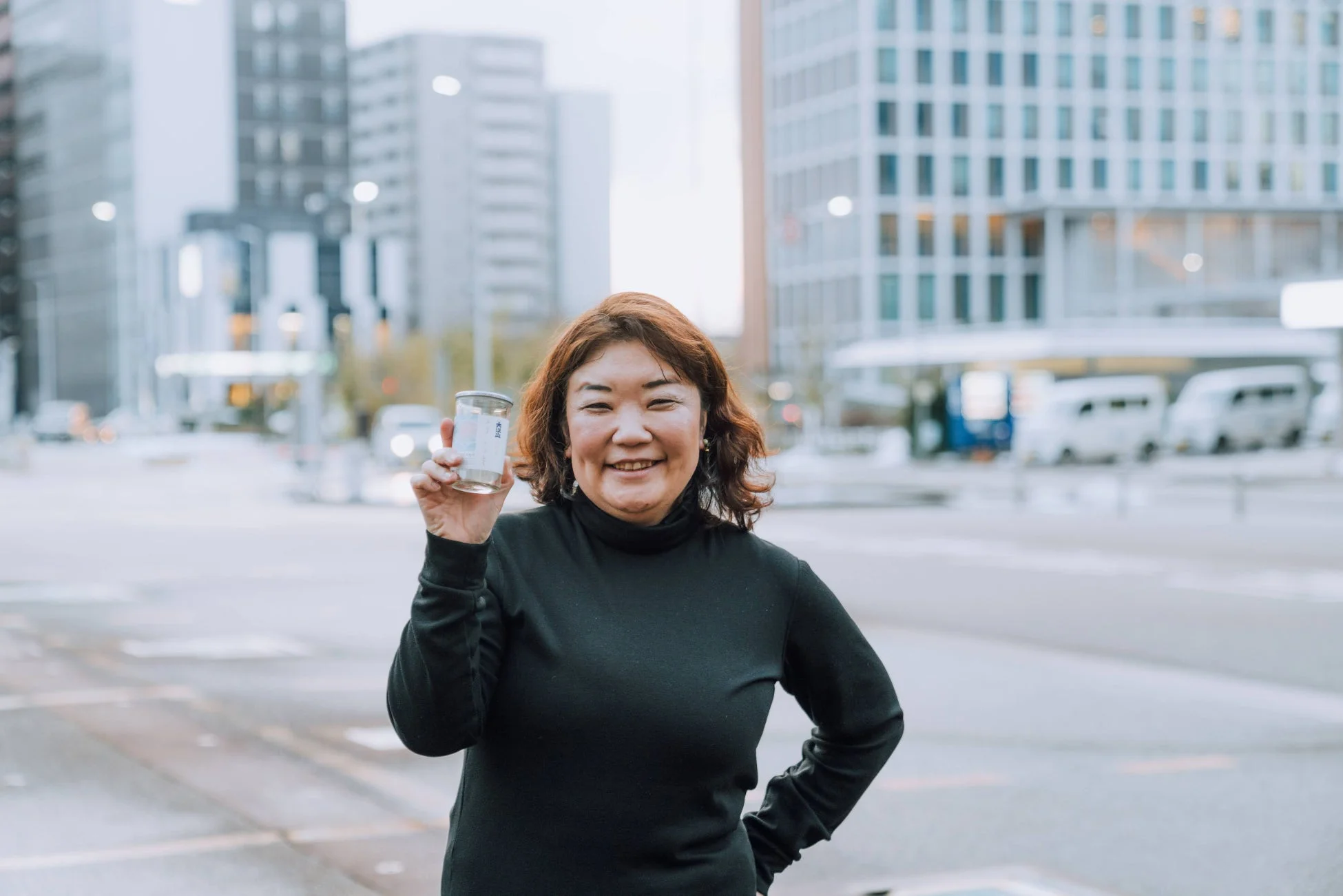 街中で笑顔の女性が小さな容器を掲げている写真