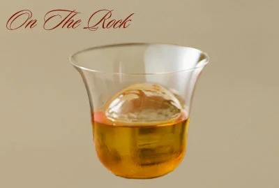 琥珀色の飲み物が入ったグラスと、その中に大きな球状の氷が浮かんでいる画像です。上部には「On The Rock」の文字があります。