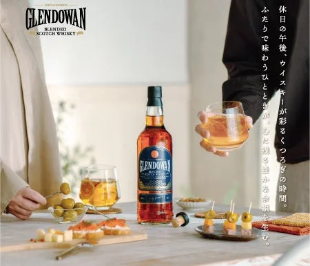 「GLENDOWAN」ウイスキーのボトルを中心に、二人がグラスを傾け、オリーブやチーズなどのおつまみと共に休日の午後をくつろいで過ごす様子を描いています。