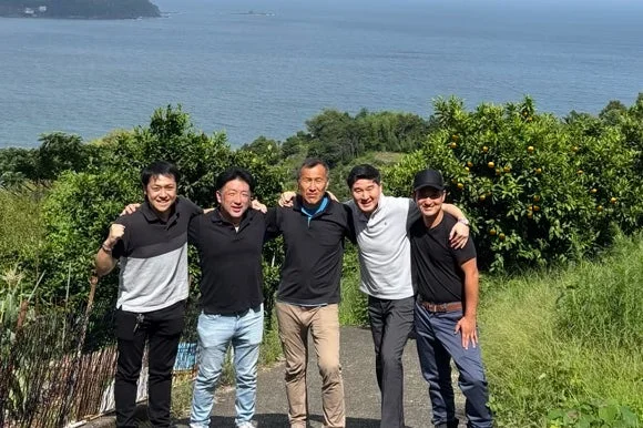 海を背景に笑顔で並ぶ男性たち