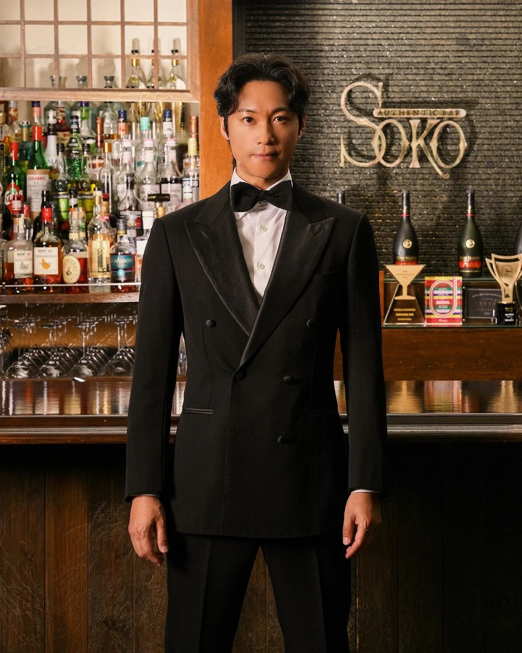 黒いタキシードを着た男性がバーカウンターの前に立つ