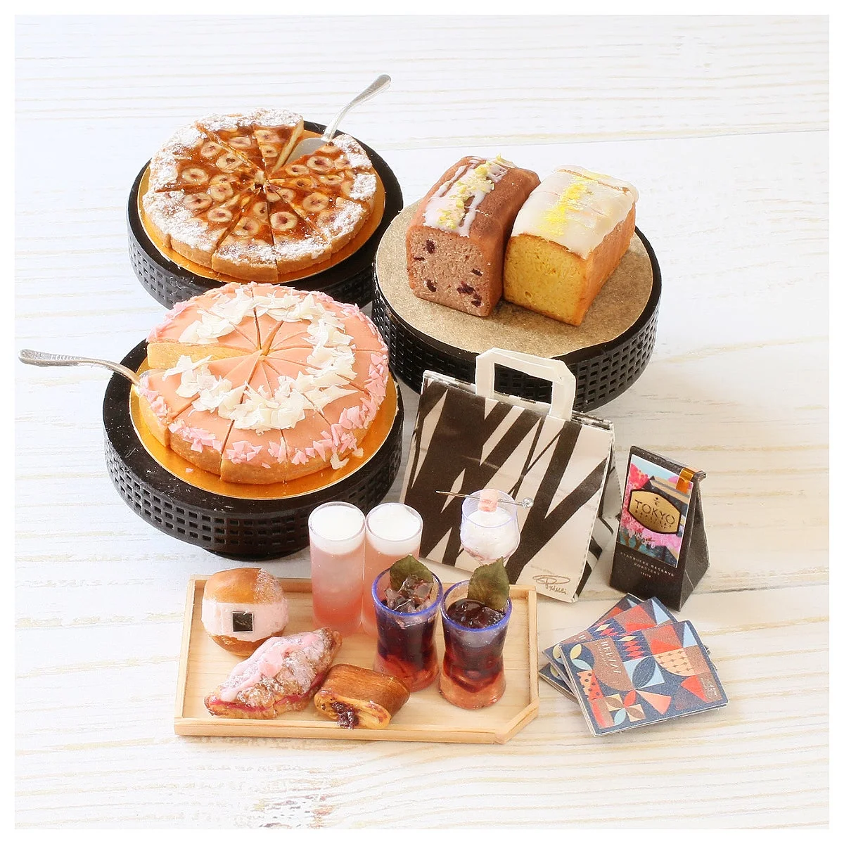 ナッツのタルトやピンクのケーキ、パウンドケーキ、クロワッサンなどの洋菓子と、数種類のドリンクが木製トレイに美しく並べられています。TOKYO COFFEEの袋も添えられた、豪華なデザートアソートメントです。