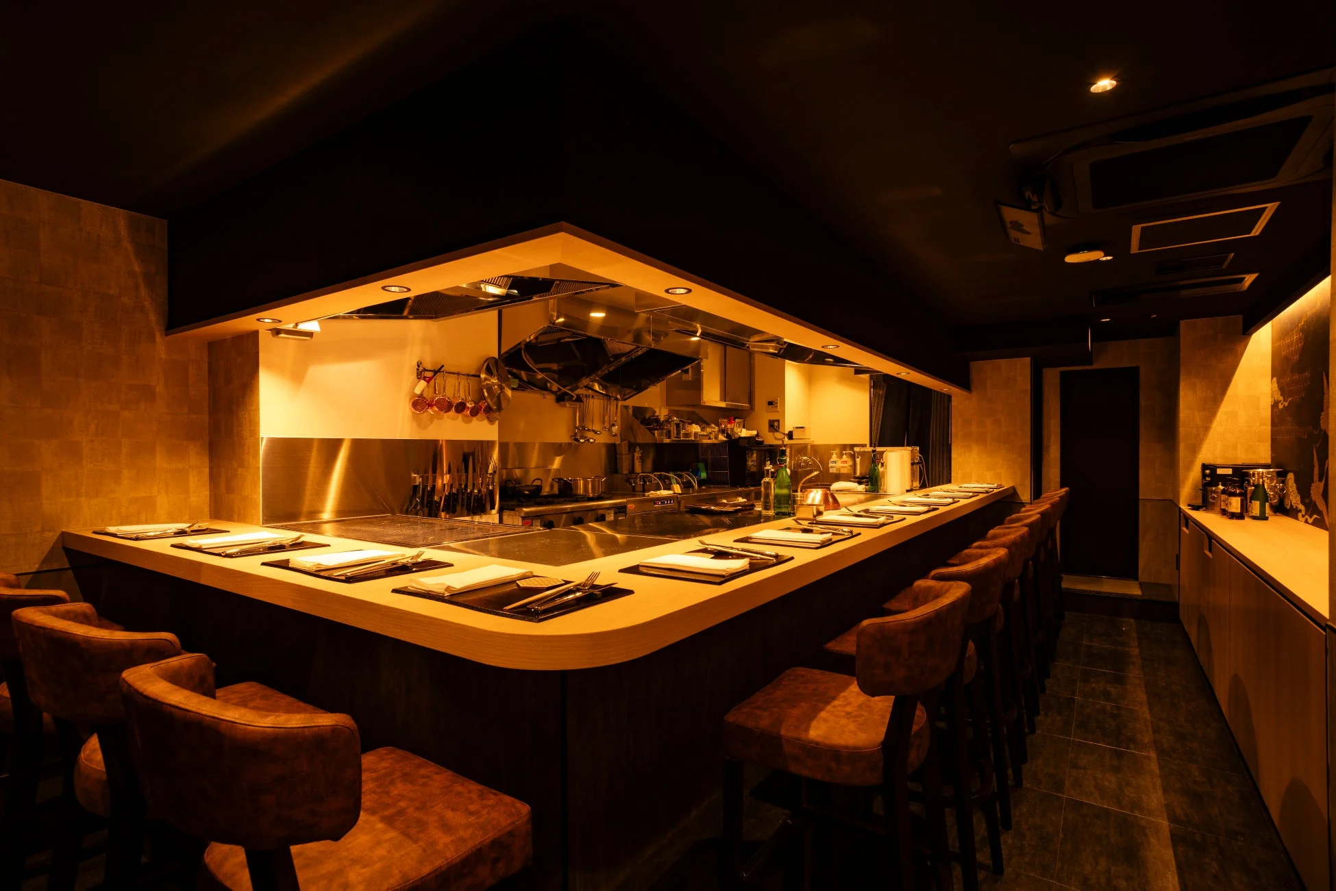 モダンで落ち着いた雰囲気のカウンター席が並ぶレストランの店内。暖色の照明が特徴で、奥には調理スペースが見えます。高級感のある内装です。