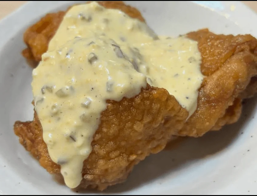 カリッと揚がったフライドチキンに、クリーミーなタルタルソースがたっぷりとかけられています。食欲をそそる一品です。