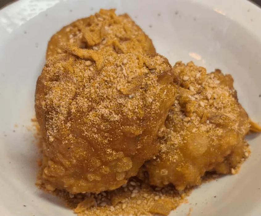白い皿に盛られた、衣がサクサクとした揚げ物が写っています。黄色い粉末調味料と白いごまがたっぷりとまぶされており、食欲をそそる一品です。