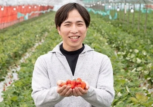 笑顔の男性がいちご農園で、両手に摘みたての真っ赤ないちごを抱える
