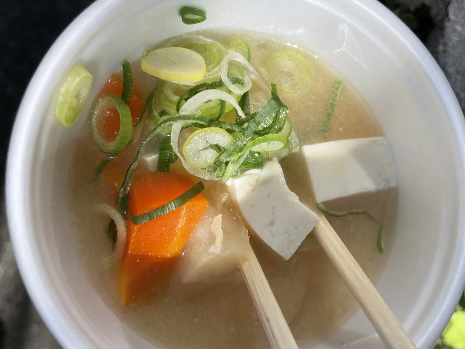白い器に入った温かい日本の汁物で、豆腐、人参、長ネギが具材として豊富に入っています
