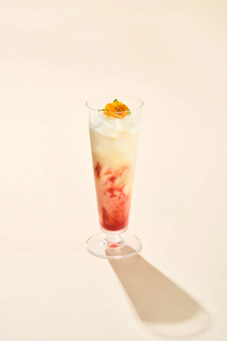 白いクリーム、薄い黄色、鮮やかな赤の層が美しいグラスドリンク