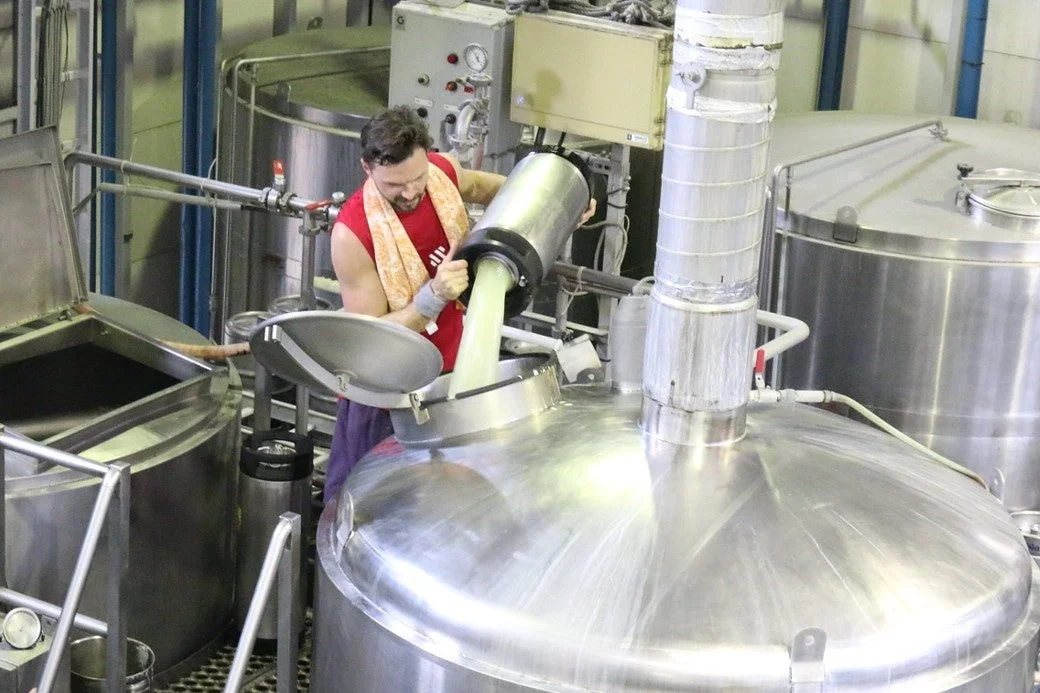 男性作業員がタンクへ薄緑色の液体を注ぎ入れている様子