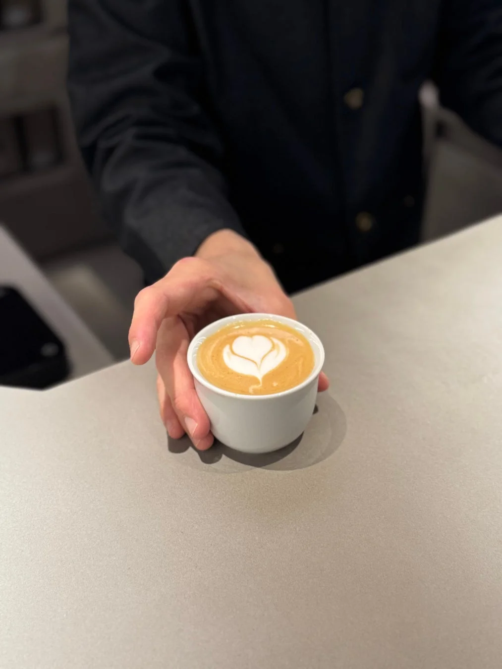 バリスタがハートのラテアートが施されたコーヒーカップを手渡ししている様子