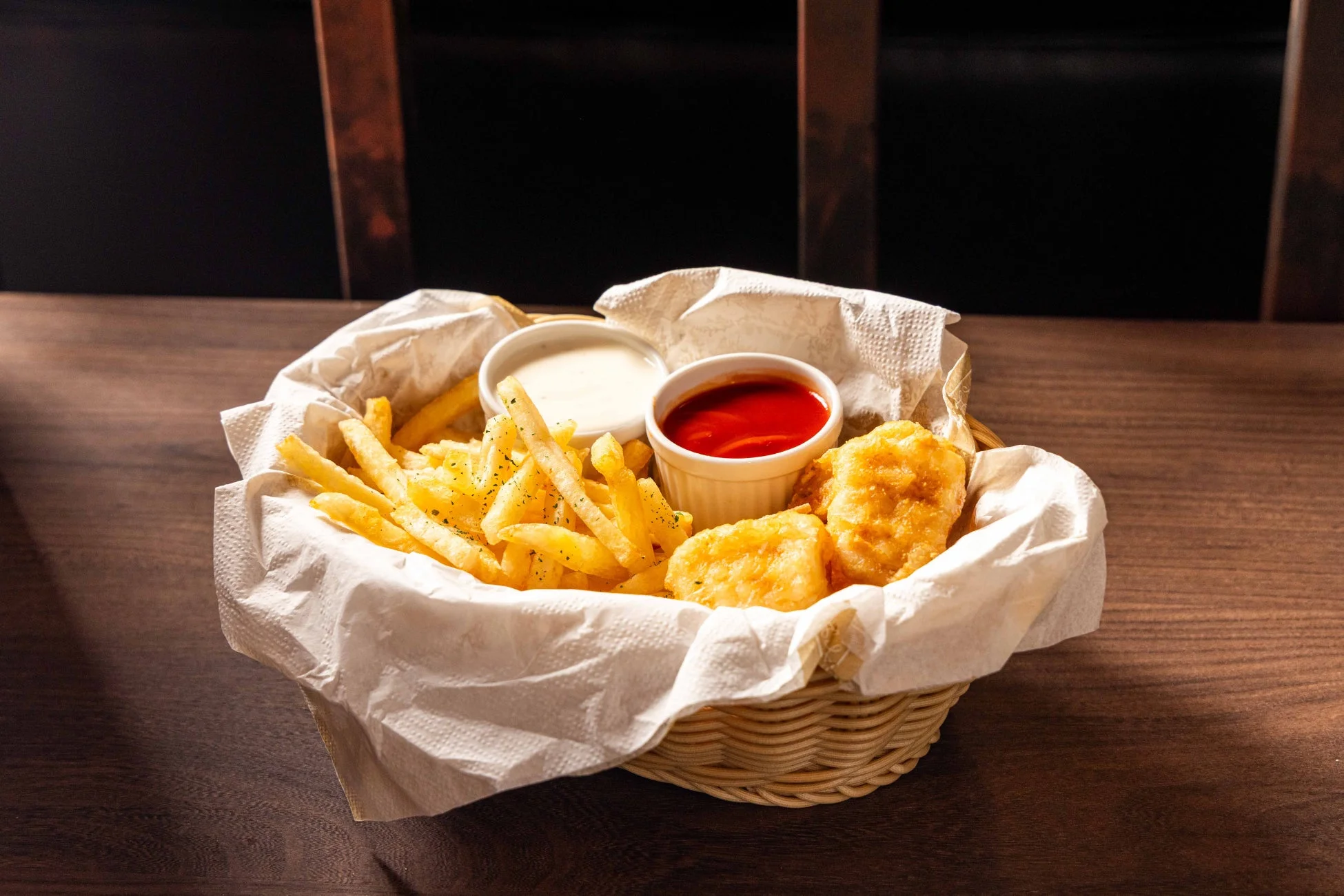 木製のテーブルに置かれたバスケットに、フライドポテトとチキンナゲットのような揚げ物が盛り付けられている