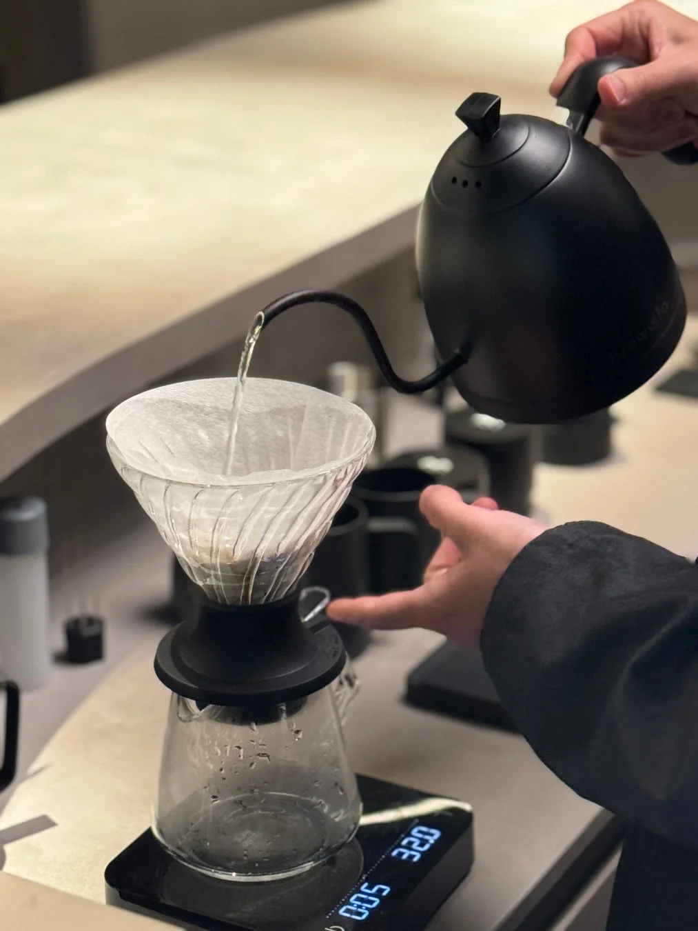 黒いグースネックケトルからお湯を注ぎ、ハンドドリップでコーヒーを淹れている様子