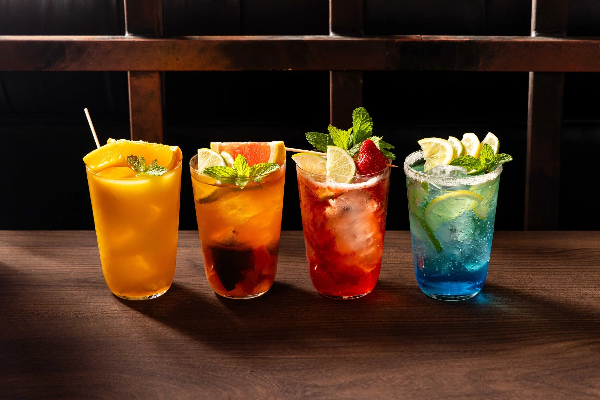 木製のテーブルに並べられた4種類のカラフルなカクテルの写真