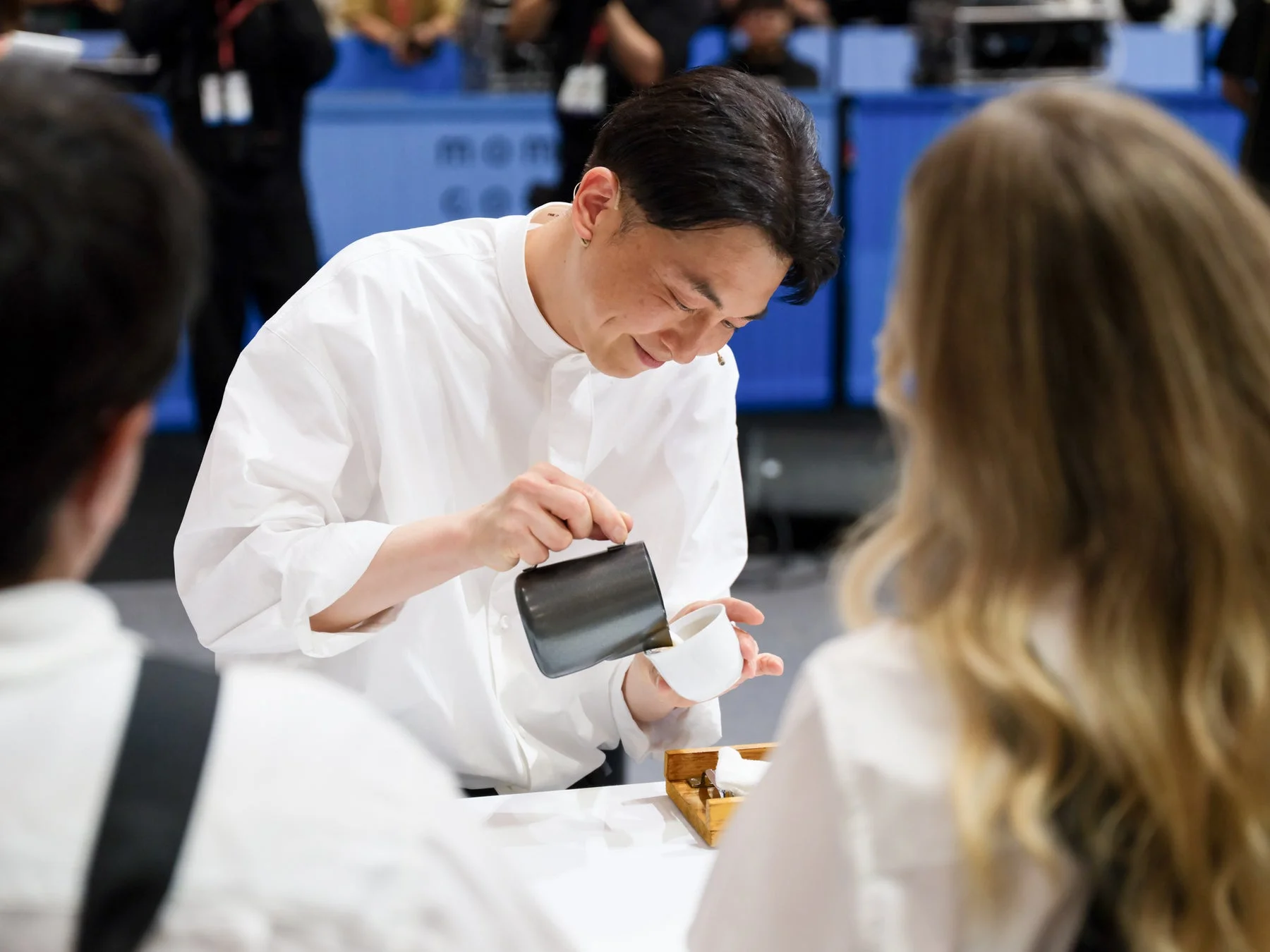 白いシャツを着た男性が、集中した表情で白いカップに液体を注いでいる様子