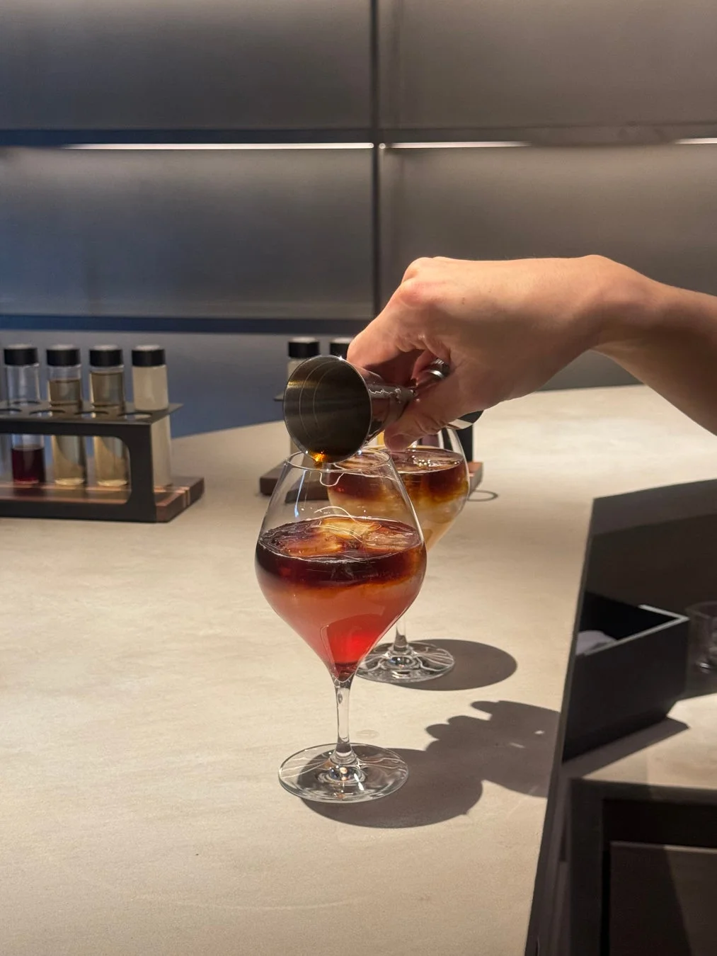 手が計量カップを使ってワイングラスにダークな液体を注いでいる様子