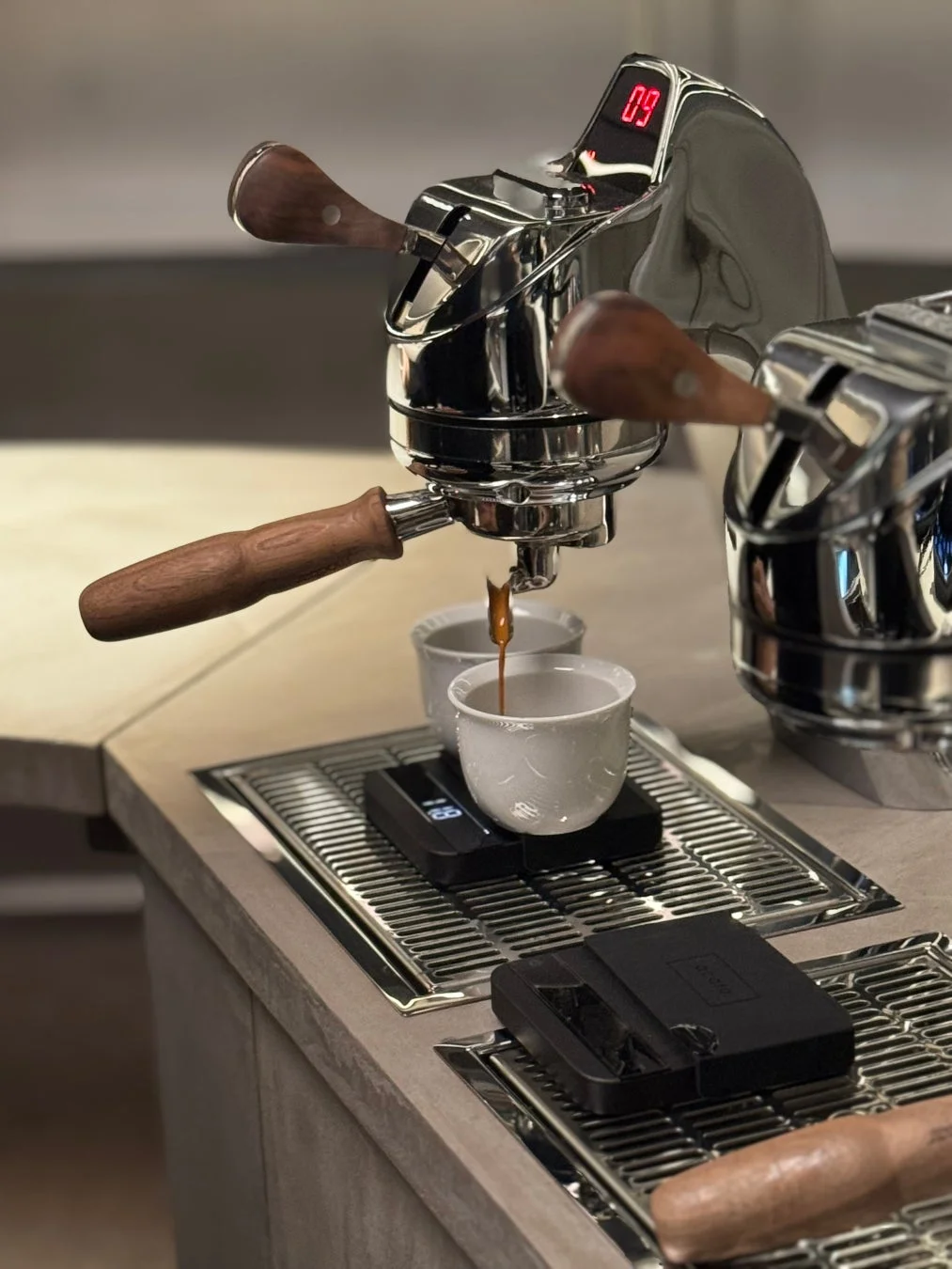 モダンなクローム製エスプレッソマシンが、デジタルスケールに乗った白いカップにコーヒーを抽出している瞬間