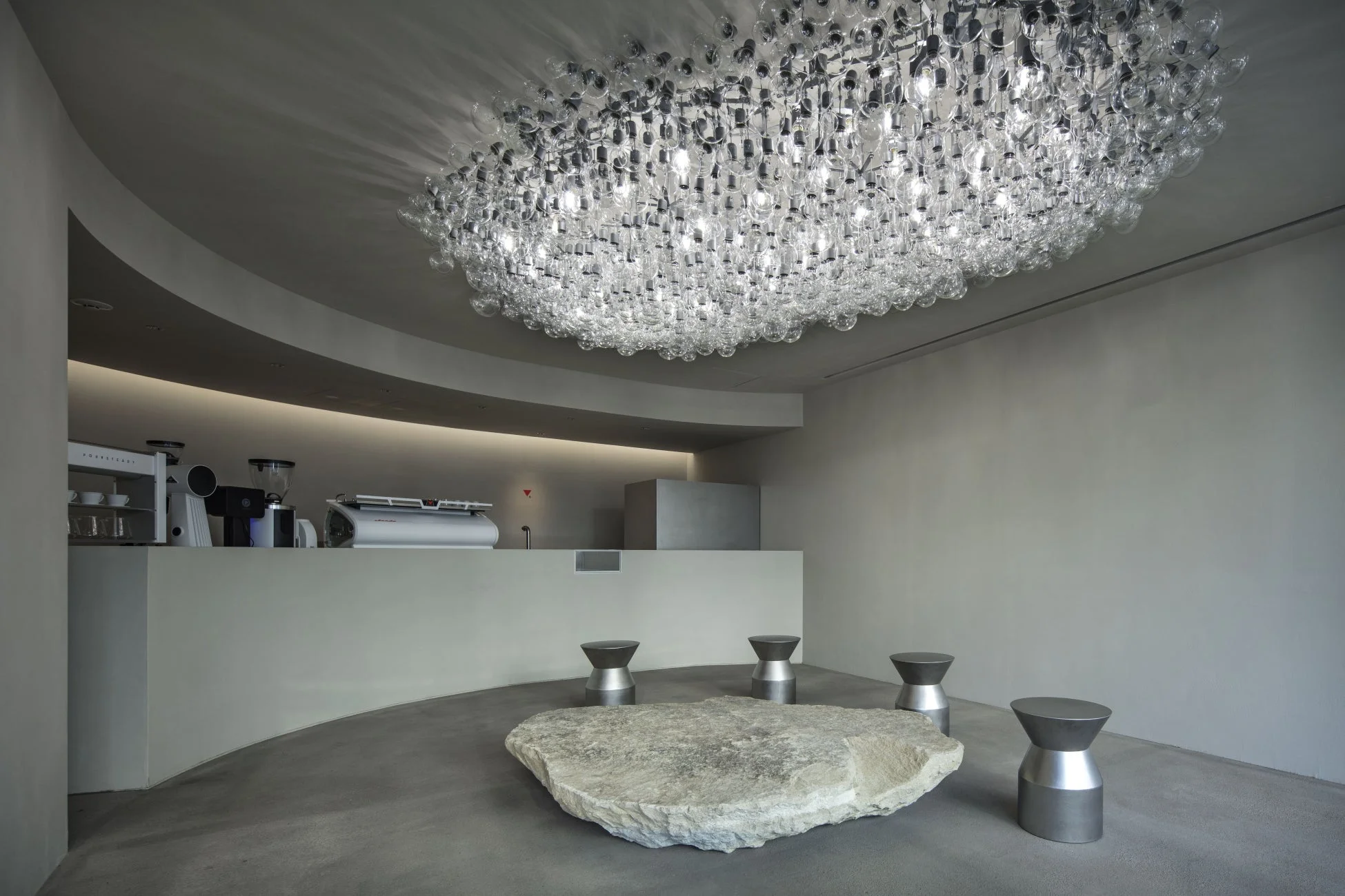 多数の電球で構成された特徴的なシャンデリアが天井に輝く、モダンでミニマルなカフェのインテリア