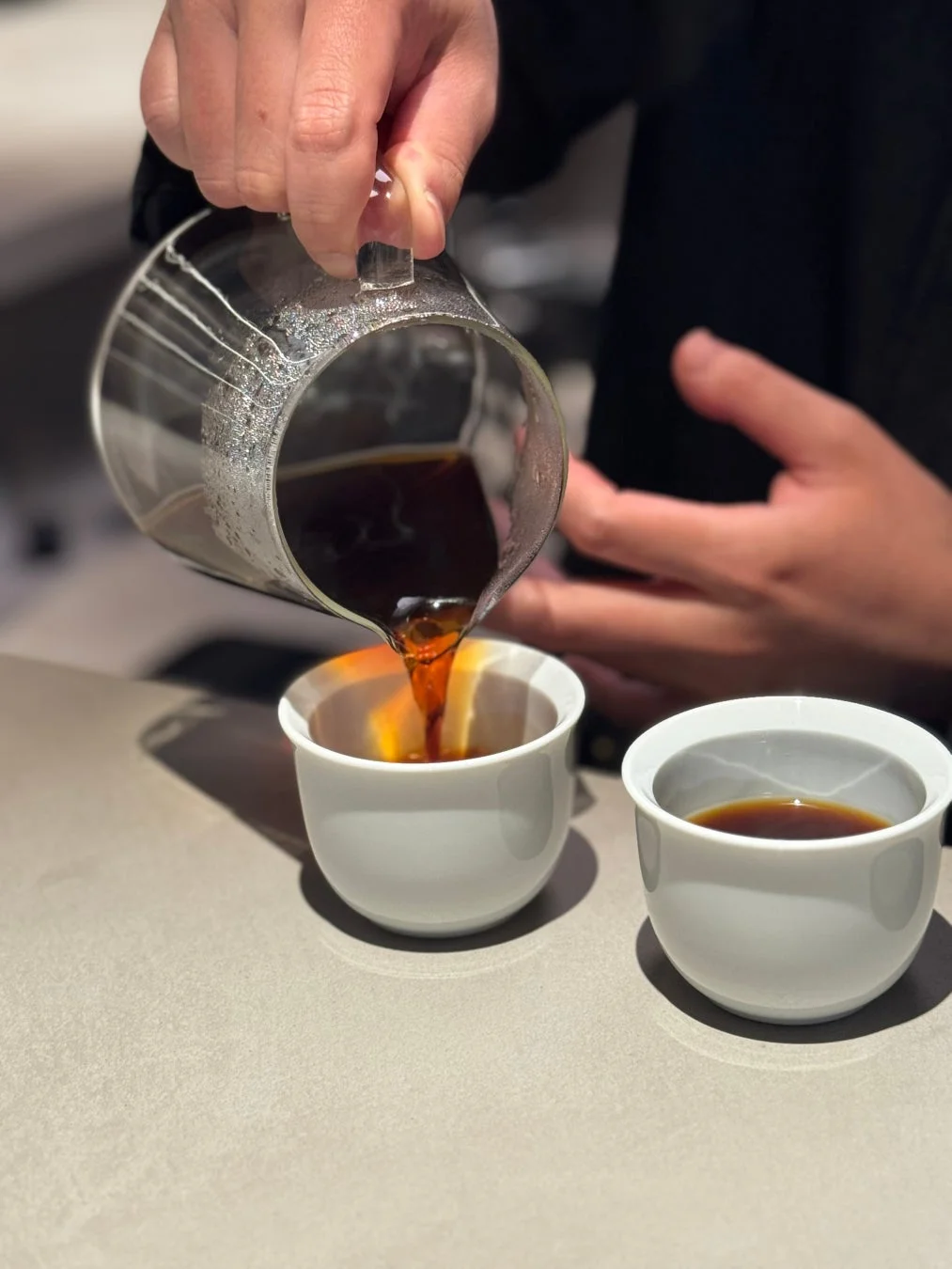 誰かがガラスのサーバーから淹れたてのコーヒーを白いカップに注いでいる様子