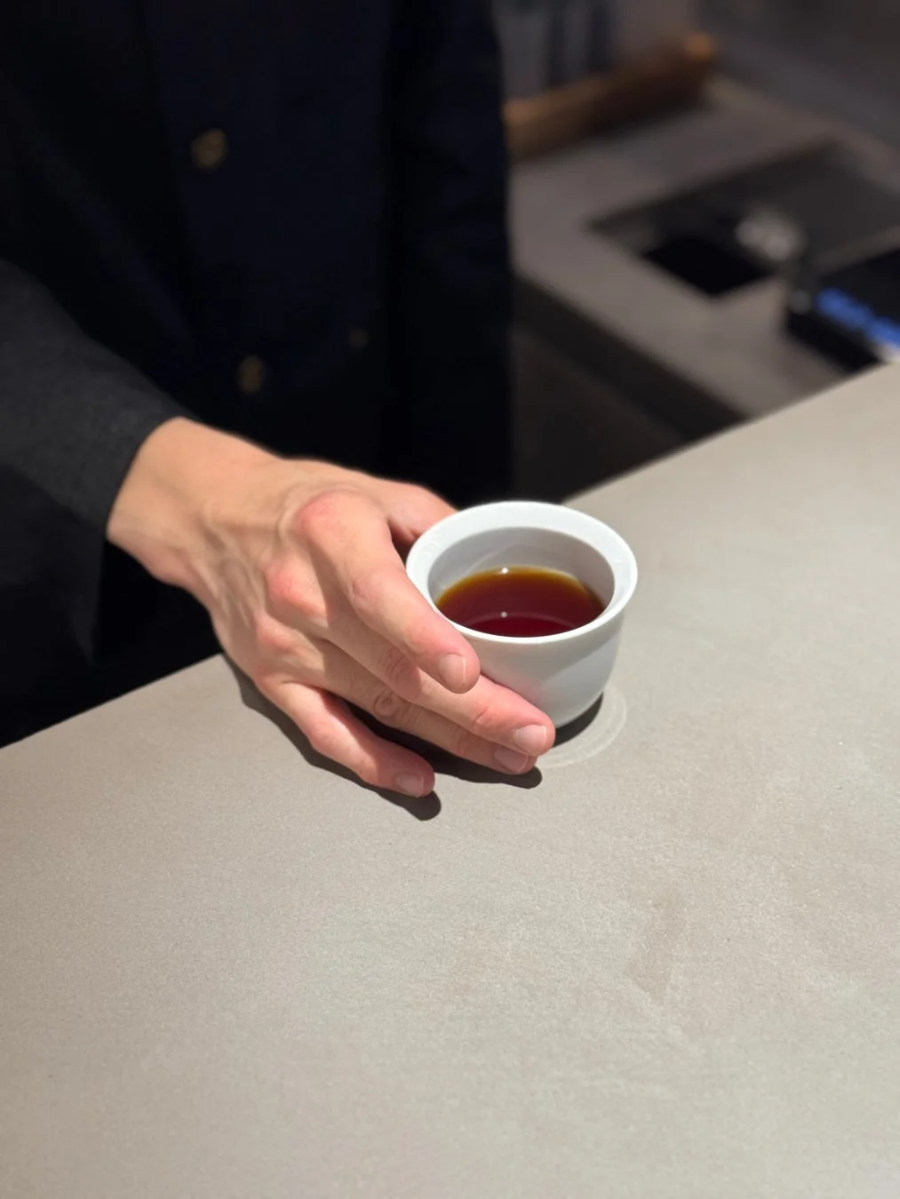 カウンターで、黒い制服を着た人物が白いカップに入った飲み物