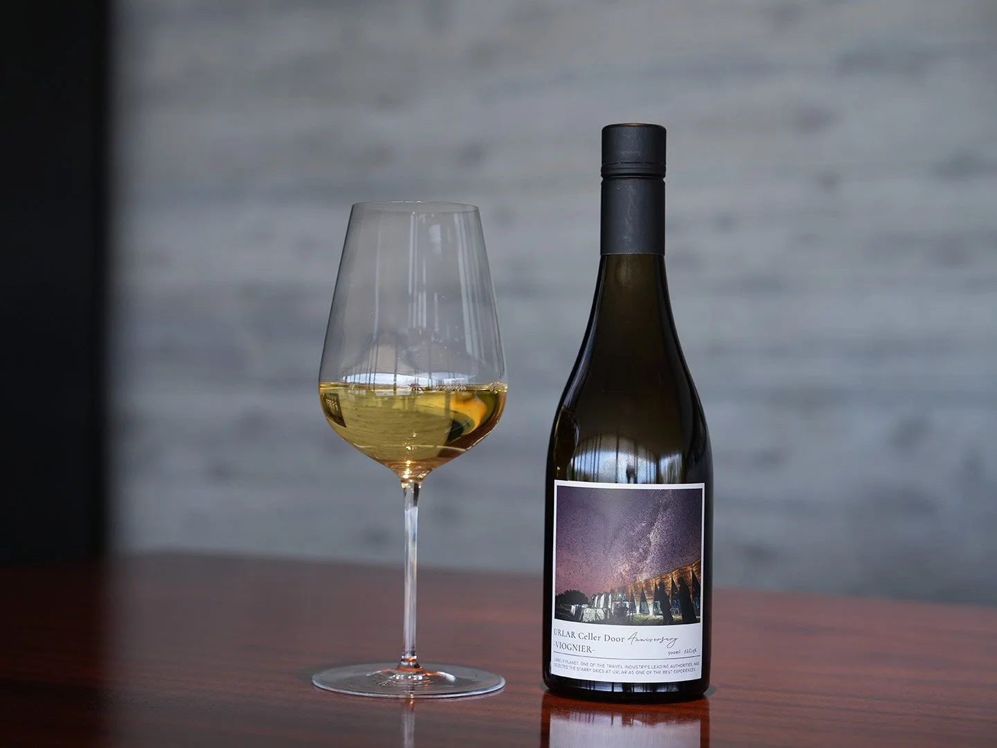 木製のテーブルの上に、黄金色の白ワインが注がれたワイングラスと、星空のラベルが特徴的なワインボトルが置かれています。洗練された雰囲気が漂う、上品な一枚です。