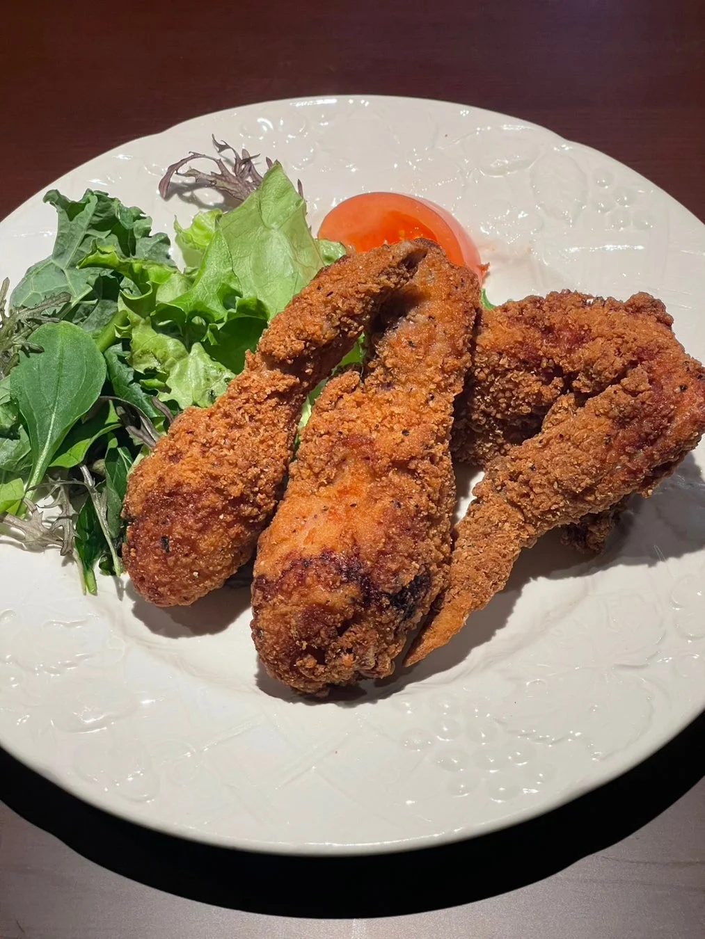白い皿に盛られたフライドチキン3個と、新鮮な葉物野菜のサラダ、トマトが添えられた料理