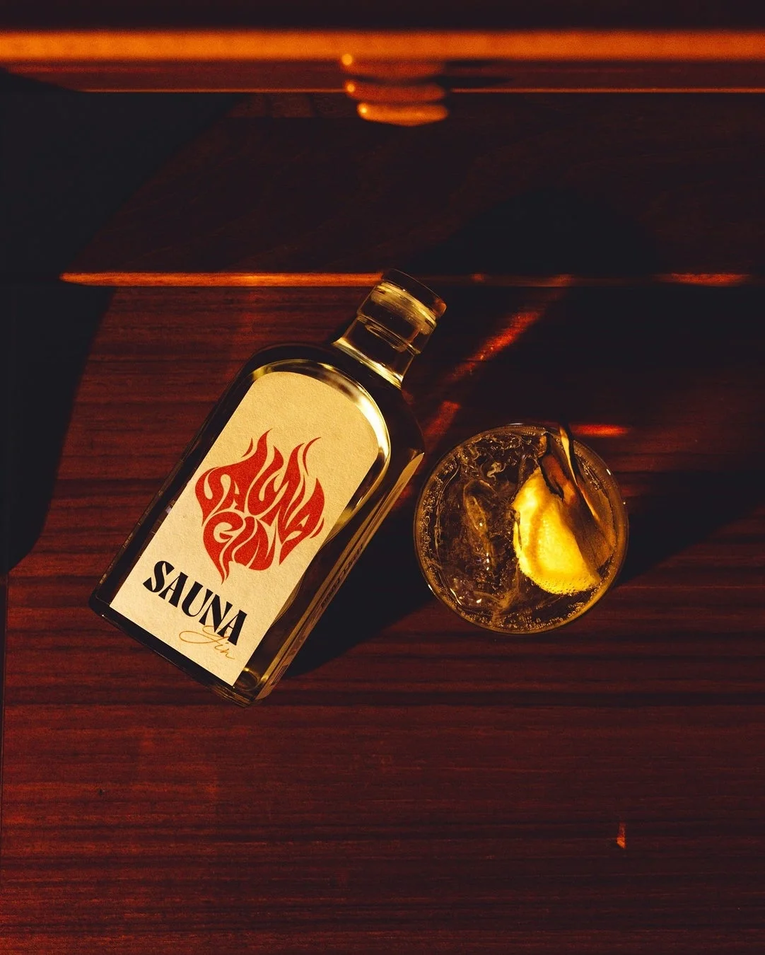 木製のテーブルに置かれた「SAUNA Jin」と書かれたボトル、そしてレモンピールと氷が入ったカクテルグラスを上から捉えた写真です。