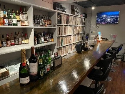 長い木製カウンターと酒瓶が並ぶ棚があるバーの店内