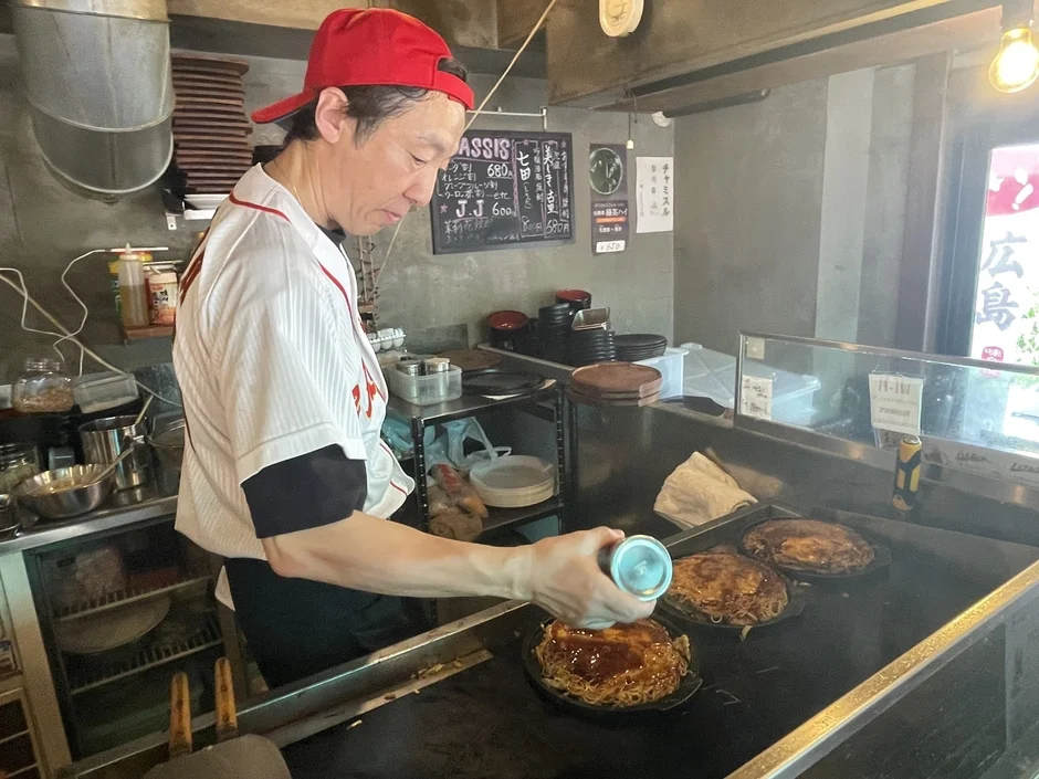 料理人がお好み焼きにソースをかけている様子