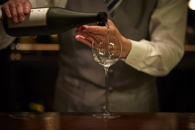 バーテンダーが日本酒「澤乃井」をワイングラスに注ぐ瞬間。落ち着いたバーカウンターで、プロフェッショナルなサービスと上品な雰囲気が伝わります。