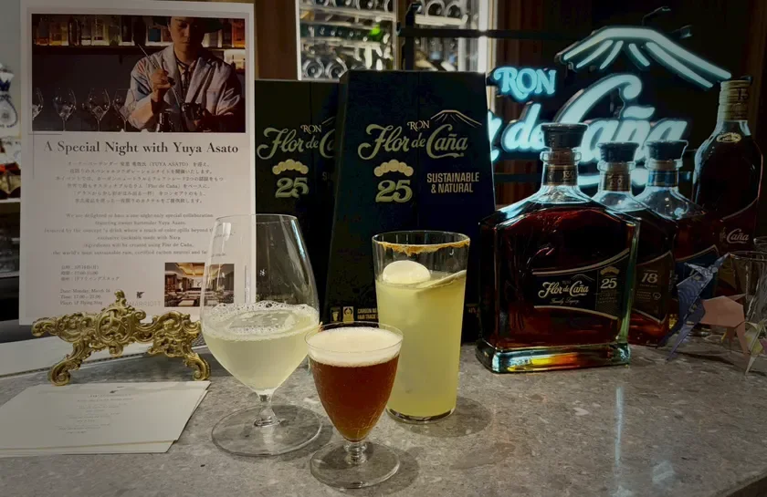 バーカウンターに「Flor de Caña」ラムのボトルとカクテルが並び、イベントの告知フライヤーが置かれています